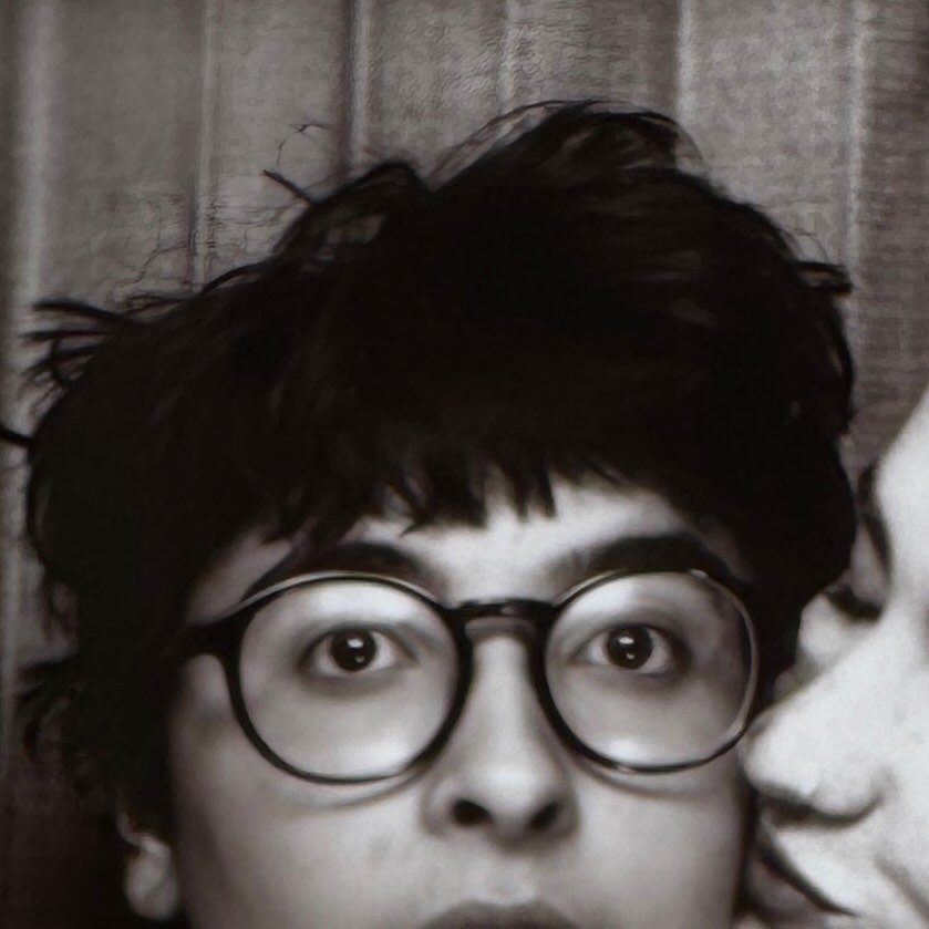 A person wearing large round glasses is kissed on their cheek