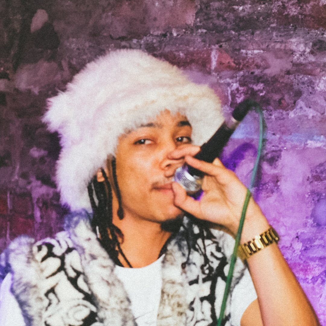 A person wearing a white fake fur hat sings into a microphone