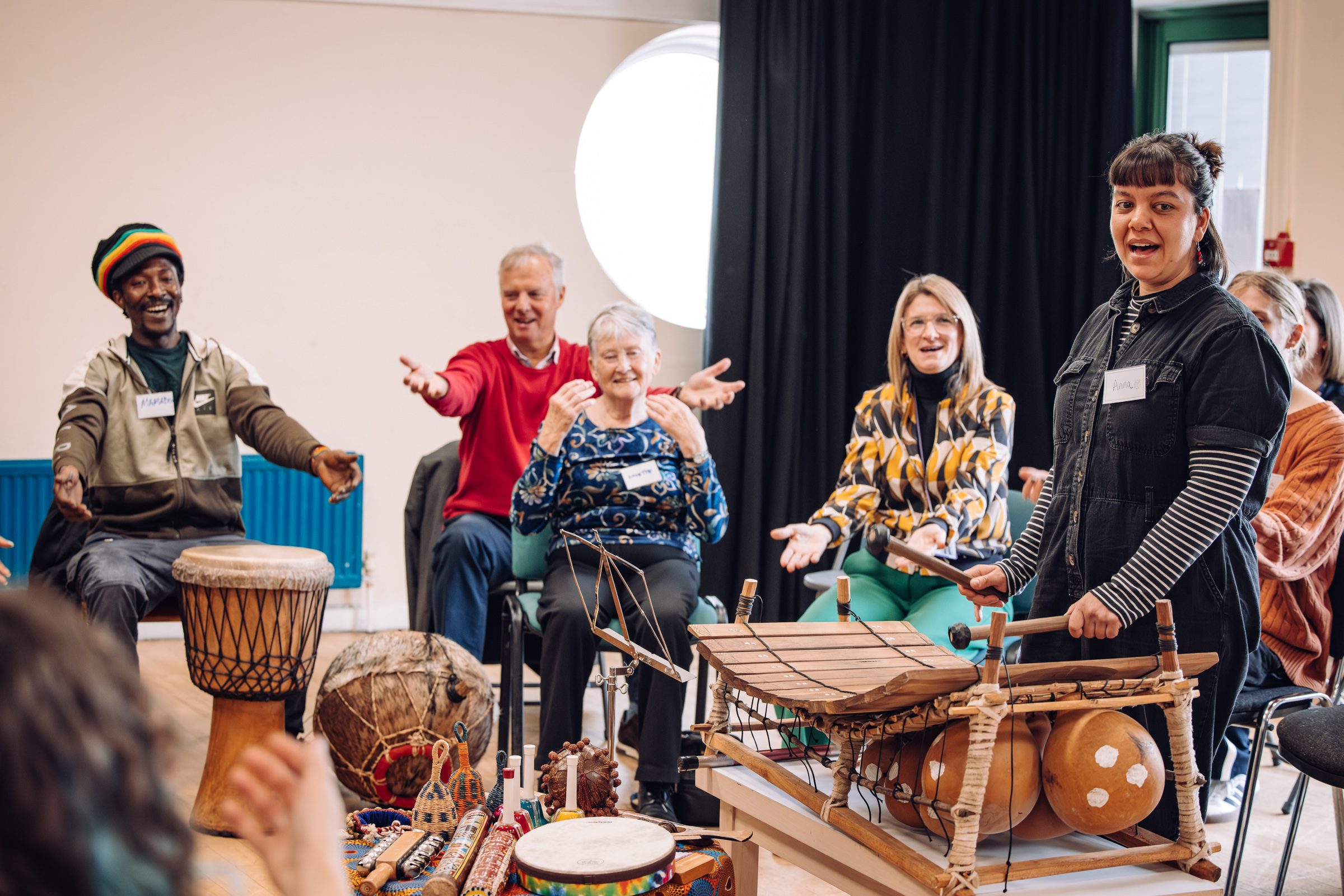A diverse group of people sit around some wooden instruments, with their arms stretched out, enjoying and playing