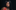 A person with a long dark hair, a fringe and tattoos