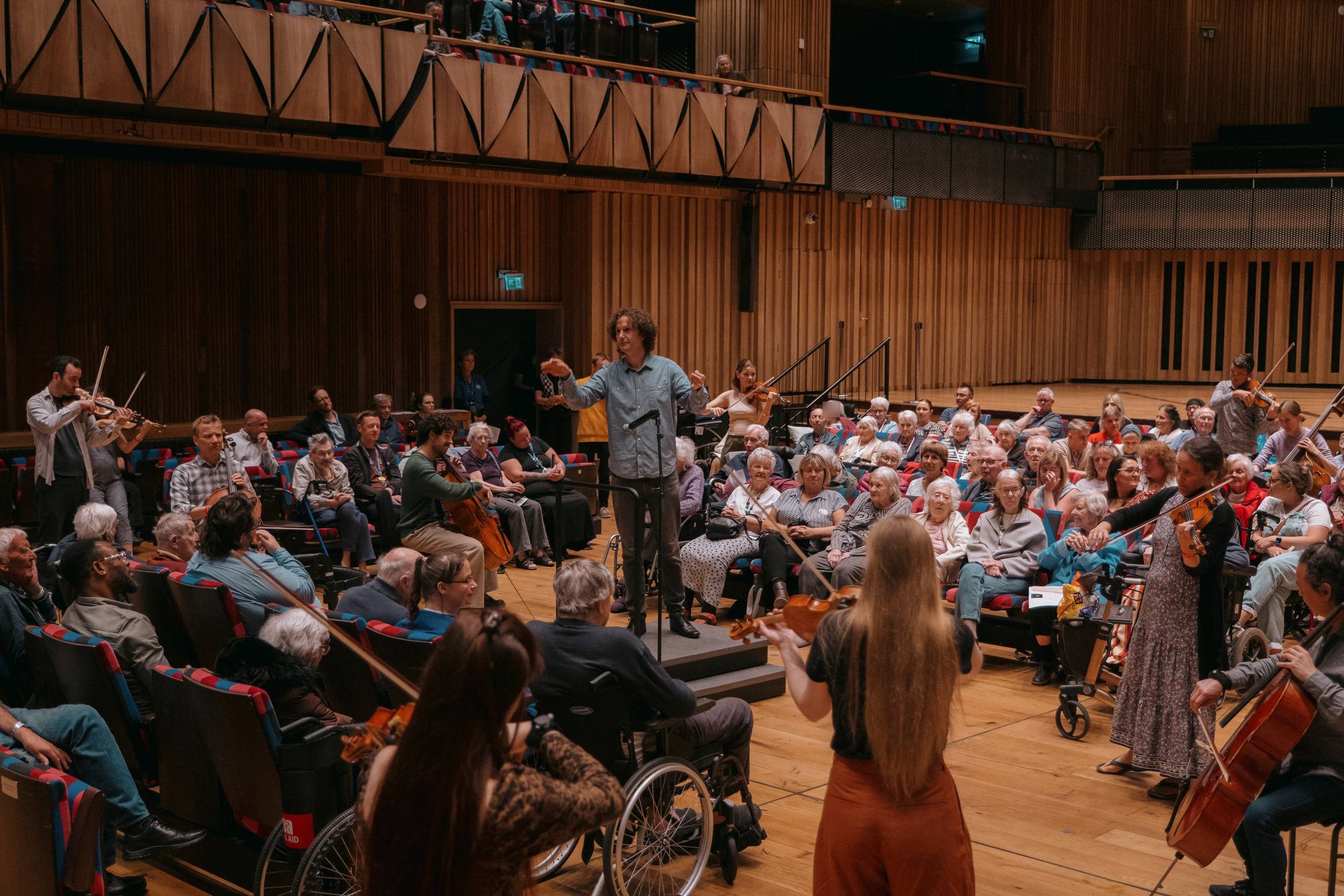 A large auditorium filled with care home residents. A conductor in blue conducts from the middle