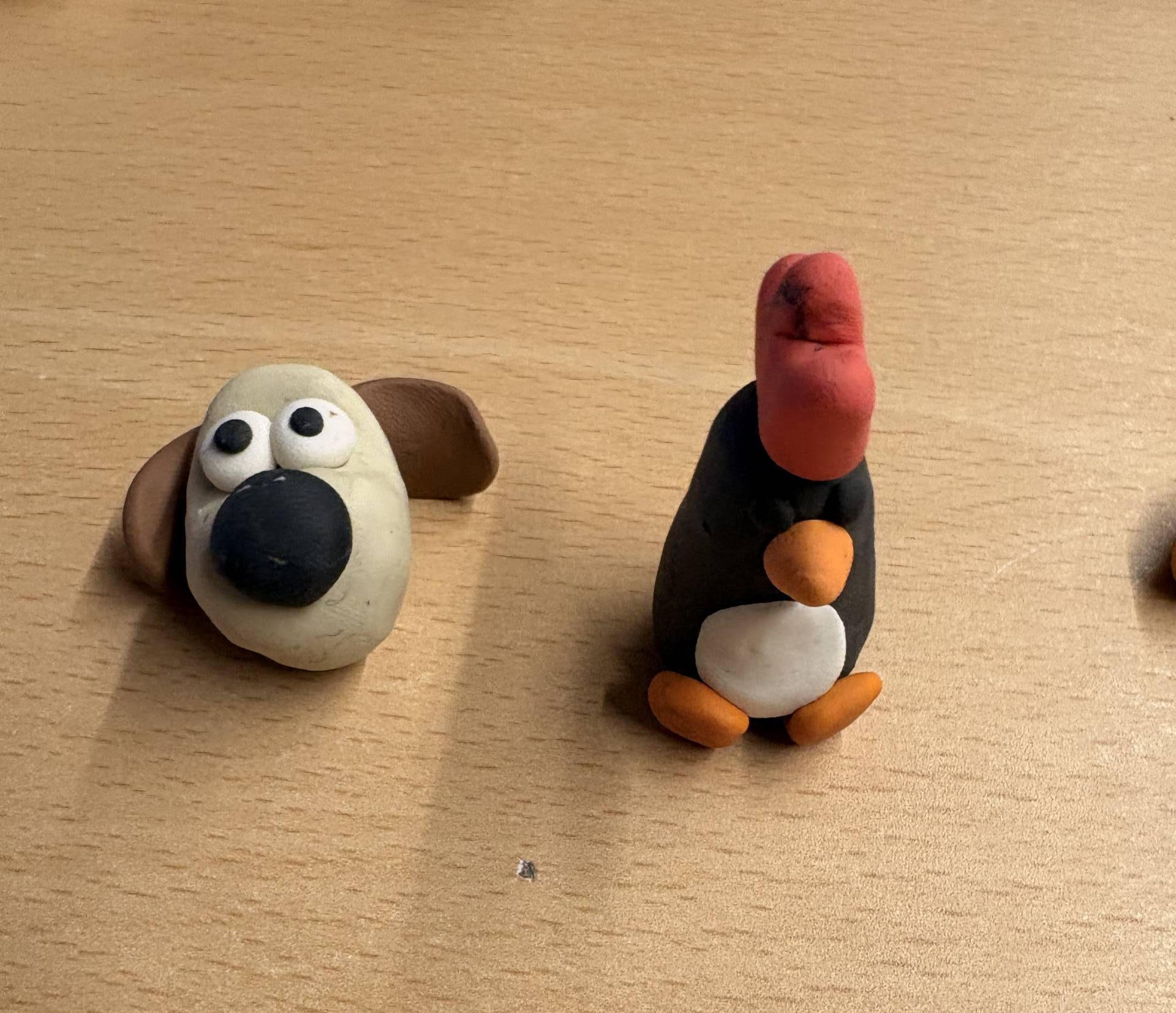 Two plastecene figures are on a table - one is Gromit from Wallace & Gromit and the other is a penguin, also from Wallace & Gromit