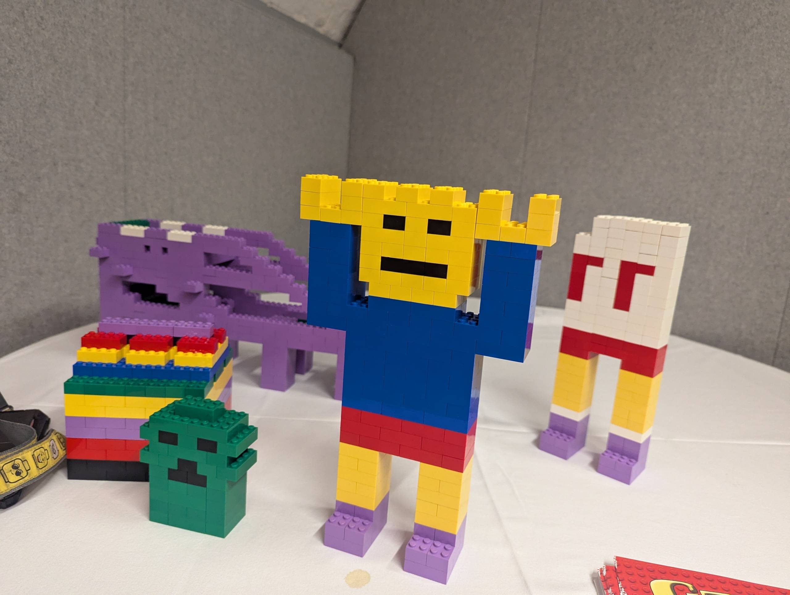 A large robot with a yellow face is constructed out of lego. Other similar constructions in bright colours are next to it