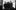A slightly blurry black a white image taken in a mirror. The mirror shows a group of four people dressed in a smart casual mirror standard outside with a leafless tree in the background.