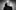 A black and white image of a person from the shoulders up, standing in front of a studio background. The have a puff sleeve, turtle neck on and have a bleach blonde up do.