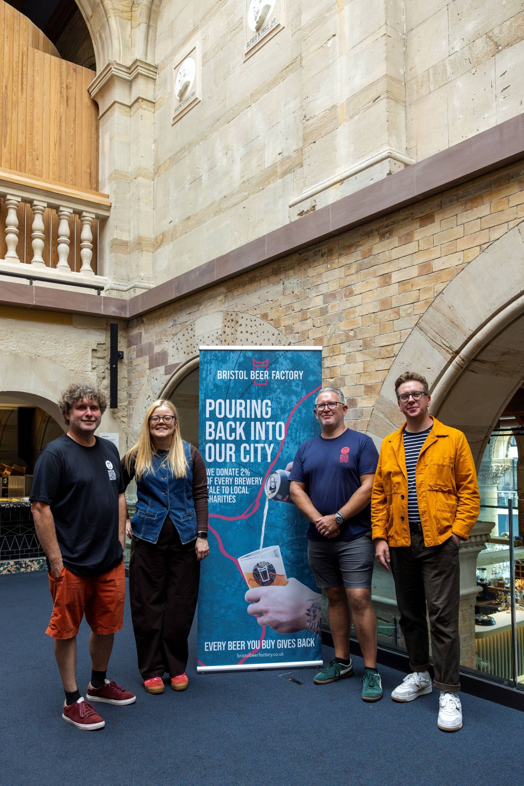 Four people standing in front of a Bristol Beer Factory banner in the Simons' Bar area of Bristol Beacon