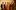 Six people stand in a line with thoughtful expressions in deep gold light.