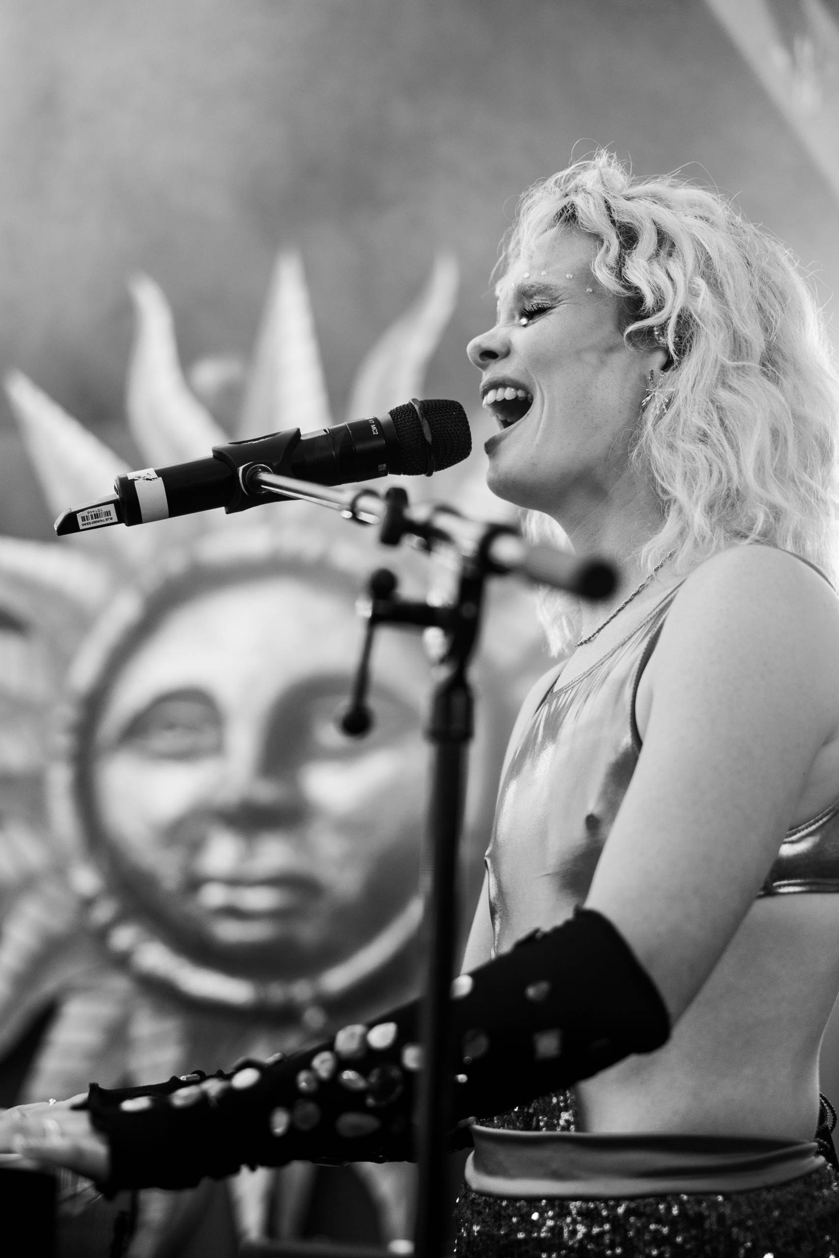 A black and white photo of a singer performing on stage in front of a large decal of a sun.
